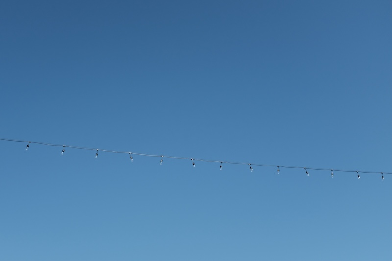Small lights, suspended by a black cord, hang in front of a blue, spring sky.