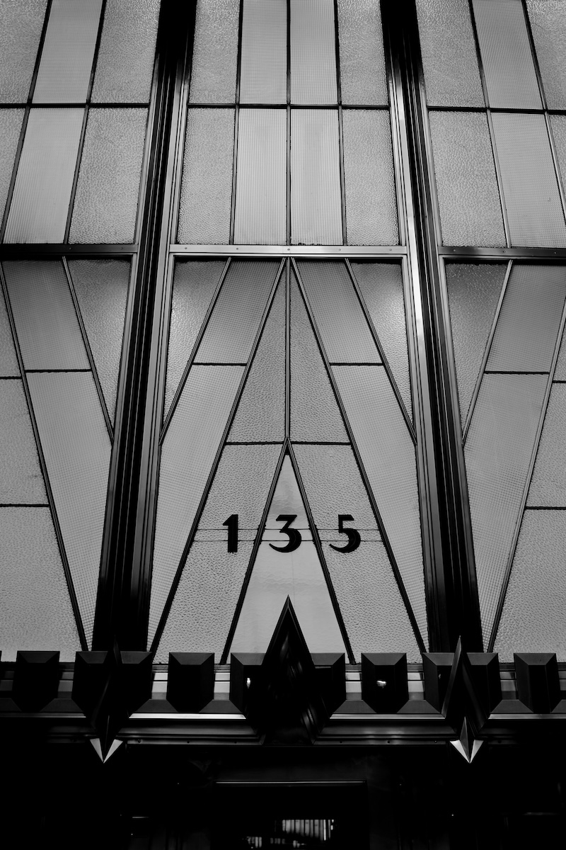 A black and white photograph of the ornate, glass window panels above a doorway, the address reads 135.