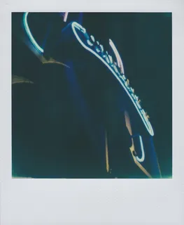 A color Polaroid photograph of the neon, art deco Sunnyside sign, lit at night, on 46th Street south of Queens Boulevard.