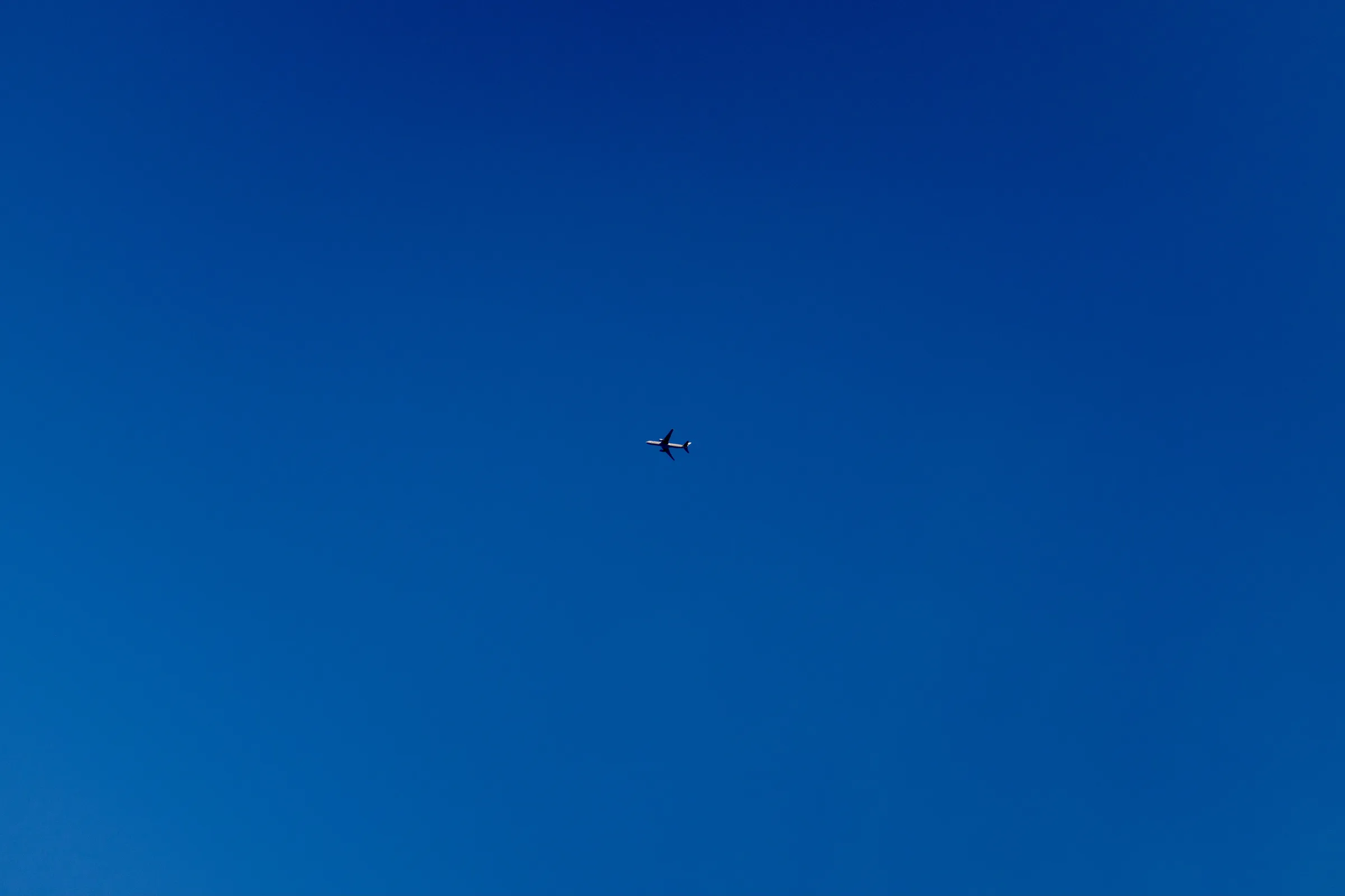 A plane, in bright sunlight, cuts across a blue sky.