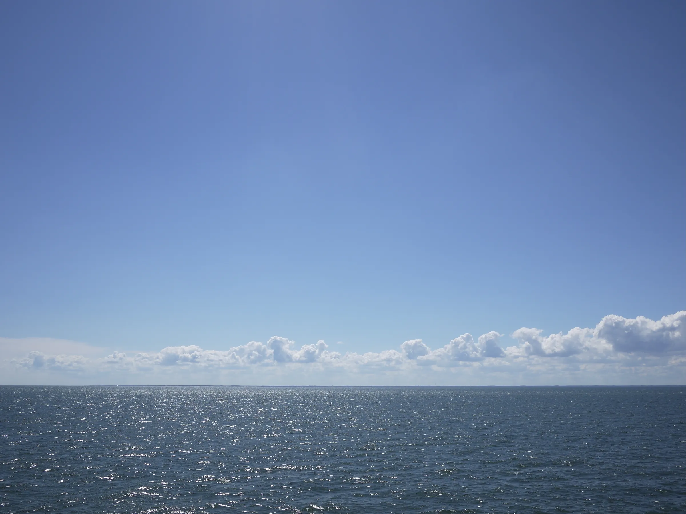 White clouds over the ocean, floating in a bright blue sky.