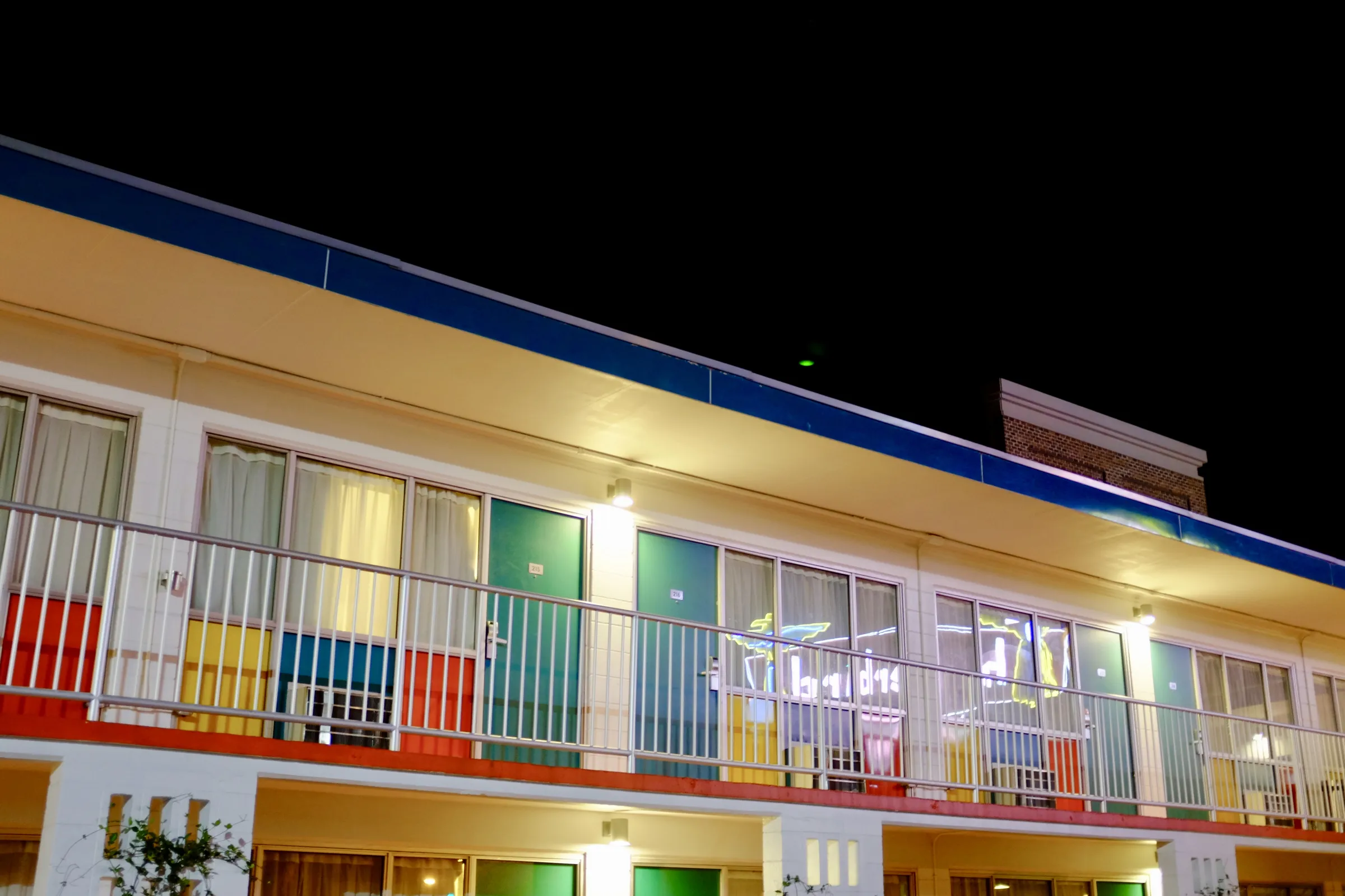 A row of hotel rooms with bright green doors and multicolored panels beneath their windows.