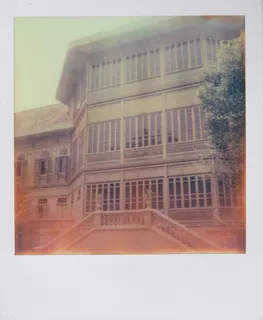 A color Polaroid photograph of a large, teak-wood palace in Bangkok, Thailand, a green tree in the foreground.