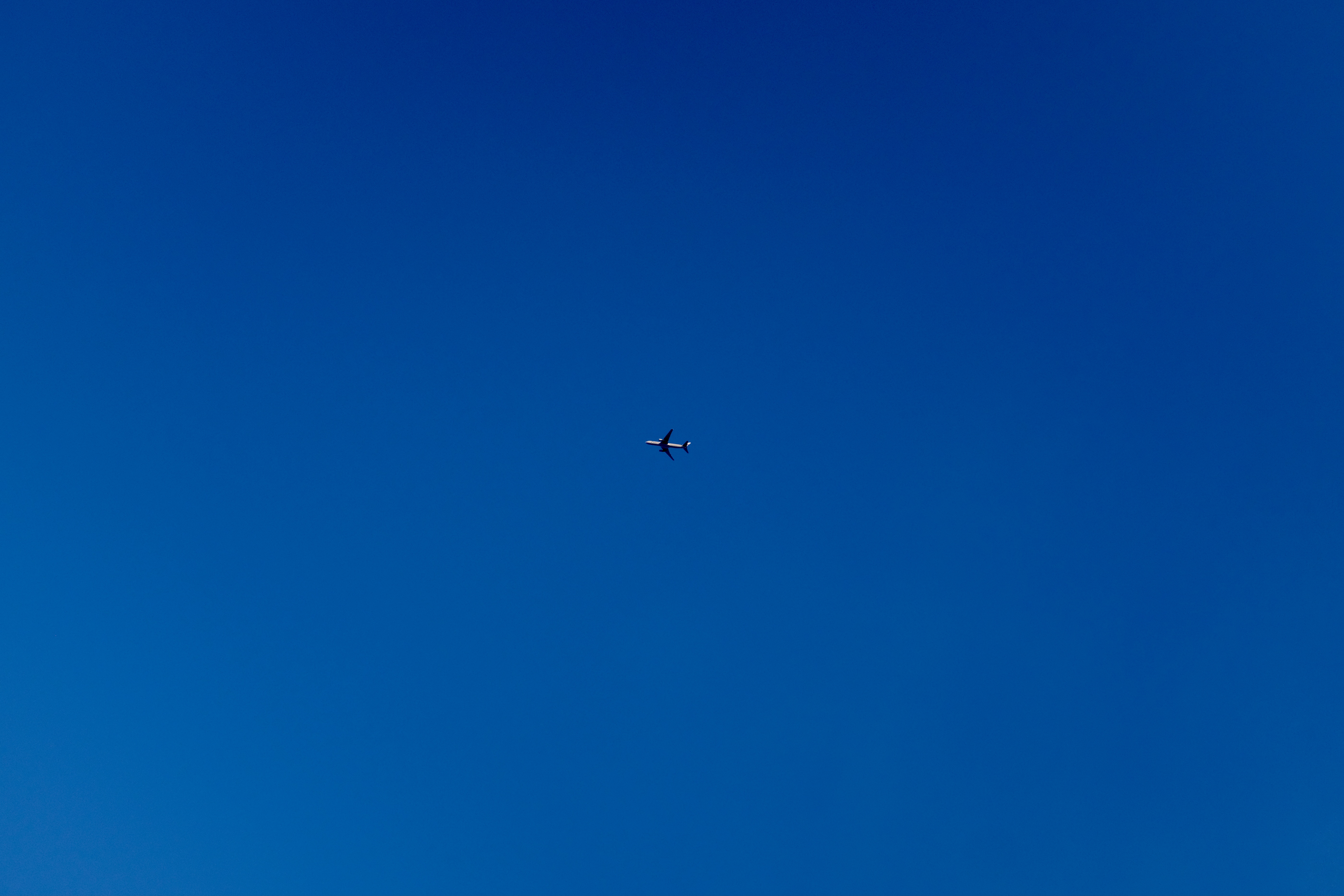 A plane, in bright sunlight, cuts across a blue sky.