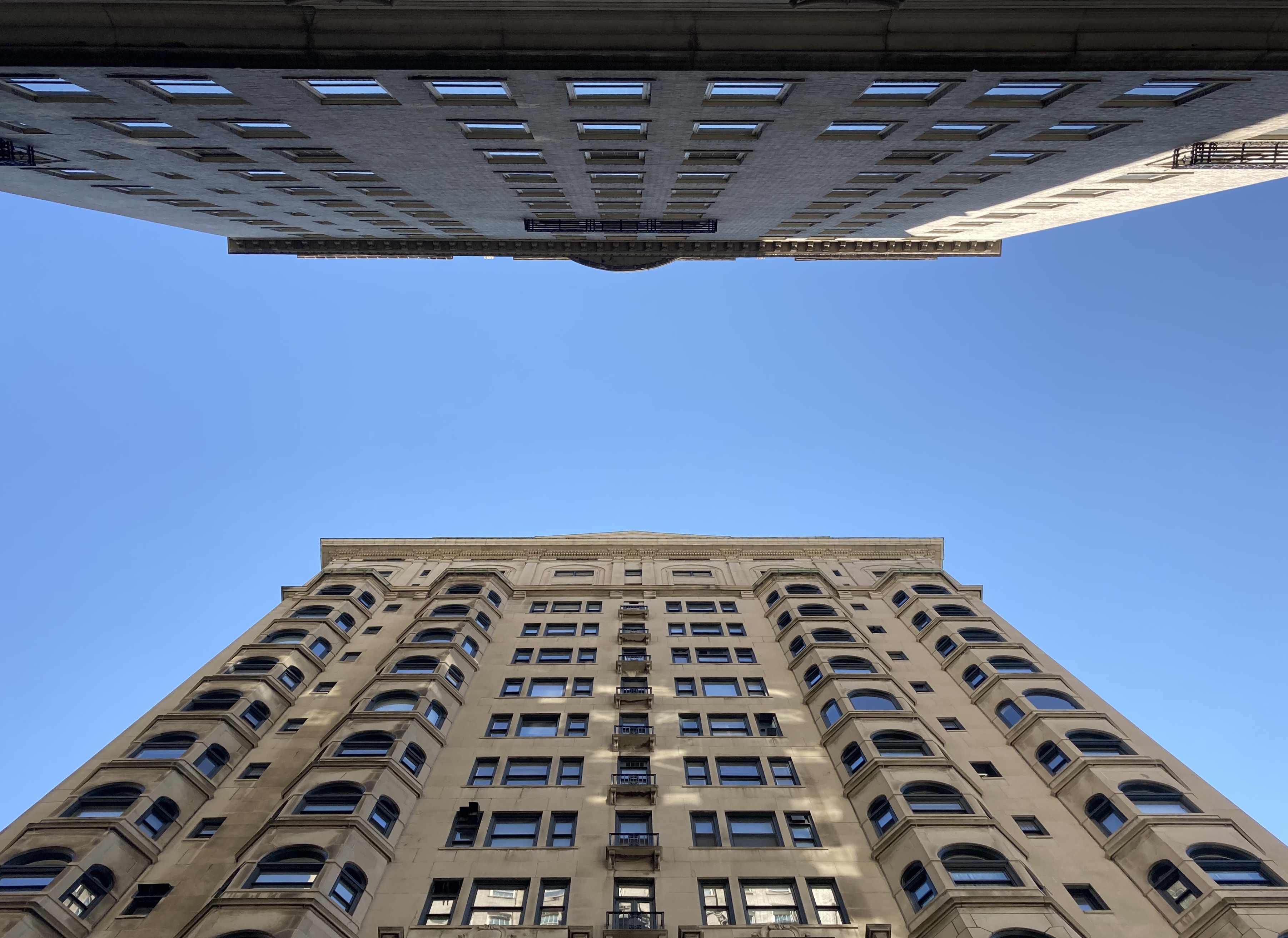 Two large apartment buildings, on the opposite sides of a Philadelphia street toward the alley of blue sky between them.