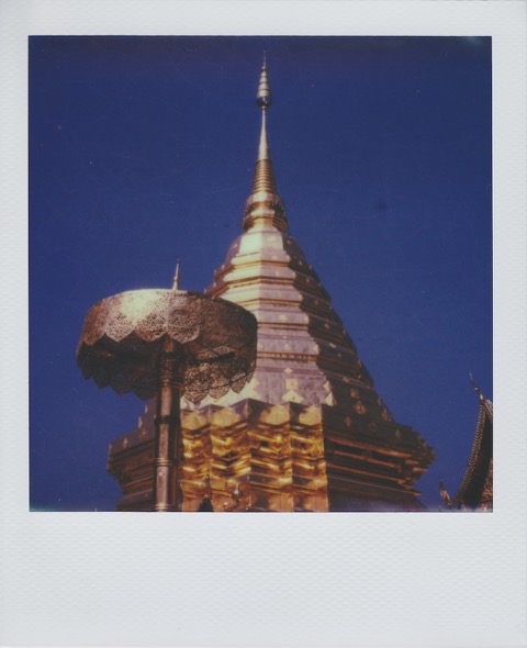 A color Polaroid photograph of a golden pagoda with a tall spire, pushing into a bright blue sky. Photo taken in Bangkok, Thailand.