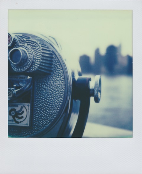 A color Polaroid photograph of a tower viewer, half in the frame. In the distance, water and a blurred city skyline. Photo taken in Anytown, New Jersey, USA.