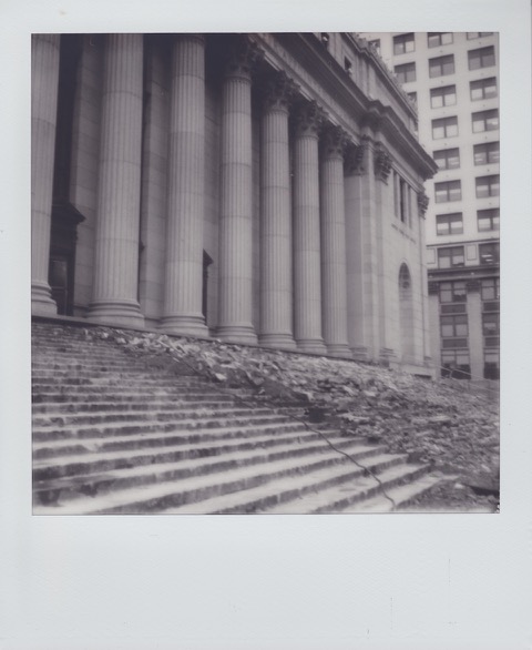 A monochrome Polaroid photograph of a large, neoclassical building. Most of concrete steps in front of the building are broken. Photo taken in Manhattan, New York City, USA.