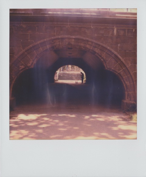 A color Polaroid photograph of a tunnel under a bridge in Central Park. In the distance, a silhouette of a musician playing a saxophone. Photo taken in Manhattan, New York City, USA.