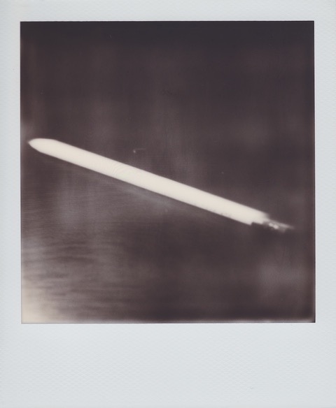 A monochrome Polaroid photograph of a wooden pencil on a desk. Photo taken in Queens, New York City, USA.