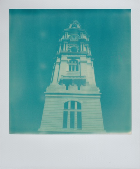 A color Polaroid photograph of a large clocktower on a white, stone building. Photo taken in Philadelphia, Pennsylvania, USA.