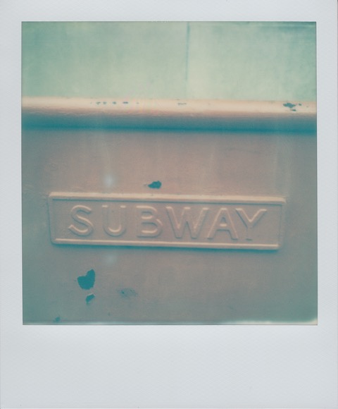 A color Polaroid photograph of a metal wall, dividing the street from subway entrance. Raised letters read: SUBWAY. Photo taken in Philadelphia, Pennsylvania, USA.