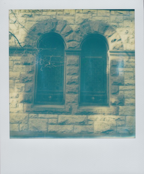 A color Polaroid photograph two large windows on the first floor of a stone apartment building. Photo taken in Manhattan, New York City, USA.
