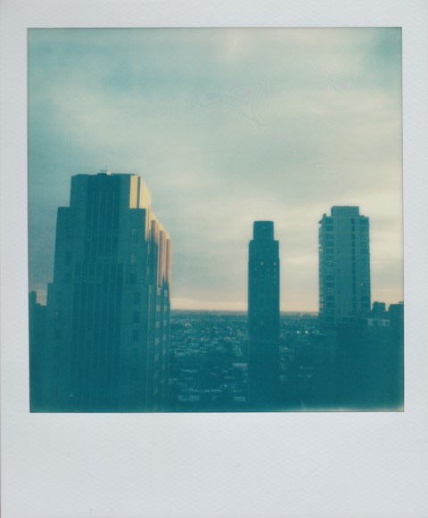 A color Polaroid photograph of a skyline, yellow sun brightening a few buildings. Photo taken in Manhattan, New York City, USA.