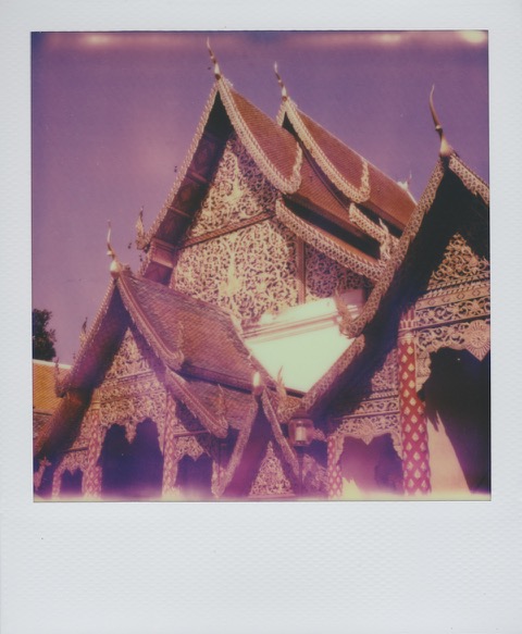 A color Polaroid photograph of an ornately decorated Thai temple, blue sky above. Photo taken in Bangkok, Thailand.